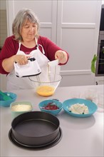 Woman chef in a white apron beating eggs in a bowl with an electric mixer to make a strawberry cake