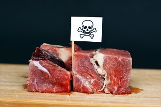 Chunks of raw meat on wooden plate with flag with poisonous skull sign