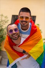 Portrait of gay male couple riding on back smiling at pride party with rainbow flag