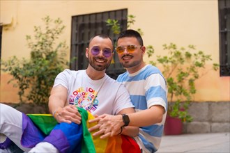 Portrait of gay male couple sitting on the floor smiling at pride party with rainbow flag