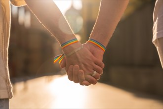 Detail of the holding hands of a couple of homosexual men with the rainbow flag at the pride party in the city at sunset