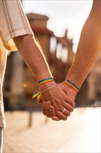 Detail of the holding hands of a couple of homosexual men with the rainbow flag at the pride party in the city at sunset