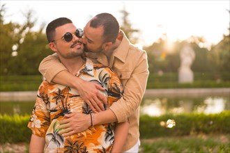 Homosexual couple embraced giving each other a kiss at sunset in a park in the city