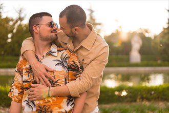 Homosexual couple embraced giving each other a kiss at sunset in a park in the city