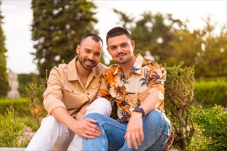 Romantic portrait of gay newlyweds sitting having fun at sunset in a park in the city