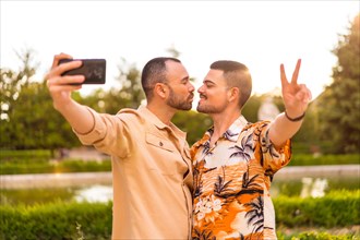 Homosexual couple taking a selfie and kissing at sunset in a park in the city
