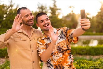 Homosexual boyfriend and girlfriend making a selfie or video call at sunset in a park in the city