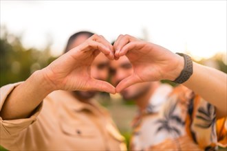 Portrait of gay boyfriend and girlfriend making heart or love gesture at sunset in a park in the city