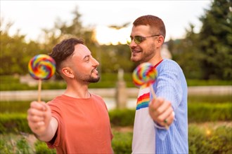 Portrait of gay wedding couple eating a lollipop in the park on sunset in the city