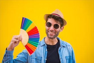 Caucasian man with a rainbow lgbt fan on a yellow background