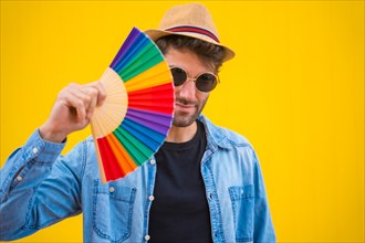 Portrait of a caucasian man with a rainbow lgbt fan on a yellow background