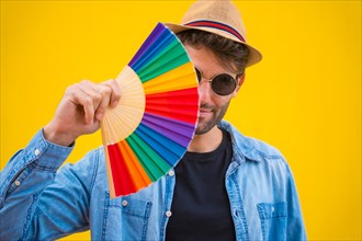 Caucasian man with a rainbow lgbt fan on a yellow background