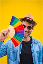 Portrait of a caucasian man with a rainbow lgbt fan on a yellow background