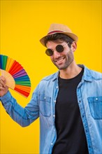 Portrait of a caucasian man in a hat with a rainbow lgbt fan on a yellow background