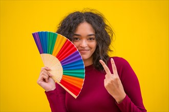 Portrait of a latin woman smiling with a rainbow lgbt fan on a yellow background