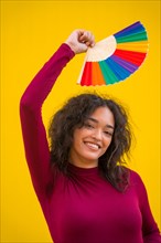 Portrait of a latin woman with a rainbow lgbt fan on a yellow background