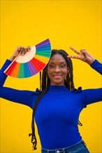 Portrait of a black ethnic woman with a rainbow lgbt fan on a yellow background