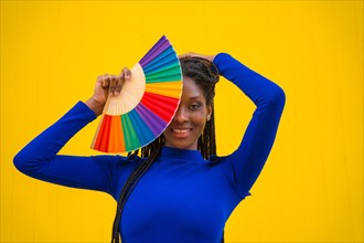 A black ethnic woman with a rainbow lgbt fan on a yellow background
