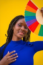 Portrait of an attractive black ethnic woman with a rainbow lgbt fan on a yellow background