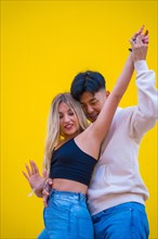 Multi-ethnic dance of an Asian and Caucasian couple dancing bachata on a yellow background