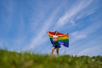 Caucasian brunette woman with a rainbow lgbt flag on the grass smiling