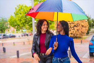 Portrait of laughing multi-ethnic female friends with an umbrella in the rain in a city