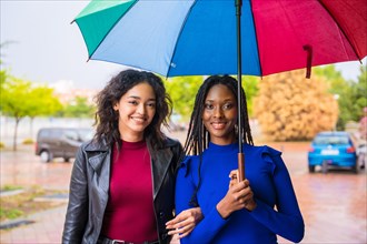 Portrait of laughing multi-ethnic female friends with an umbrella in the rain in a city in spring