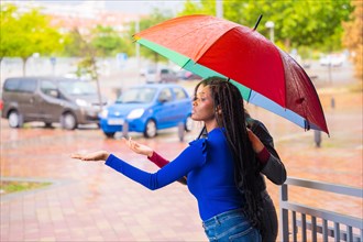 Multi-ethnic female friends with a rainbow umbrella in the rain in a city