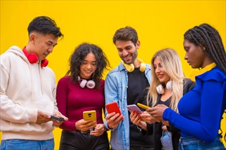 Low angle view of a group of young multi-ethnic teenage friends using cell phones on a yellow background