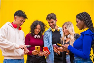 Low angle view of a group of smiling young multi ethnic teenage friends using cell phones on a yellow background