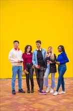 Portrait of a group of smiling young multi-ethnic teenage friends using cell phones on a yellow background