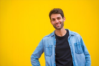 Portrait of an excited handsome man in basic clothes smiling isolated over yellow background