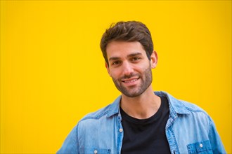 Portrait of a handsome excited model man in basic clothes smiling isolated over yellow background