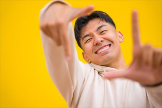 Portrait of south korean man in basic clothes over yellow background having fun and making take photo gesture