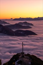 View of the summit cross and the surrounding sea of fog shortly in front of sunrise in autumn at Herzogstand