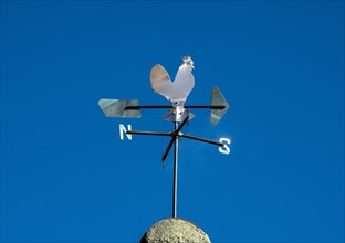 Weathercock in the shape of a rooster on a blue sky
