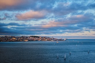 View of Lisbon over Tagus river from Almada with yachts tourist boats at sunset with dramatic sky