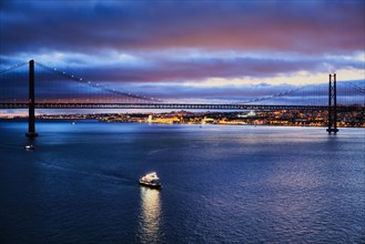 View of 25 de Abril Bridge famous tourist landmark of Lisbon connecting Lisboa and Almada on Setubal Peninsula over Tagus river in the evening twilight with tourist boats
