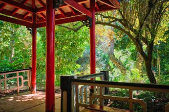 Red Chinese style pavilion in lush greenery of asian part of tropical botanical garden in Lisbon