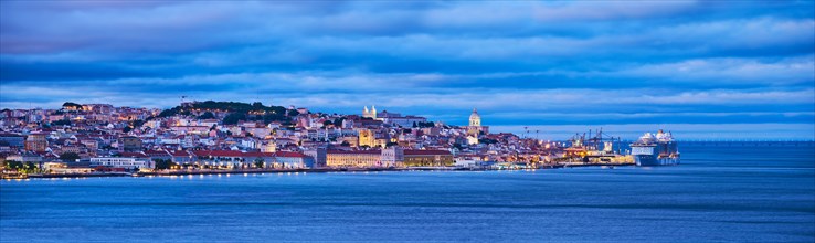 View of Lisbon over Tagus river with passing ferry boat from Almada with moored cruise liner in evening twilight