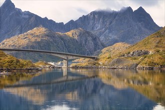 A bridge and high mountains reflected in a fjord