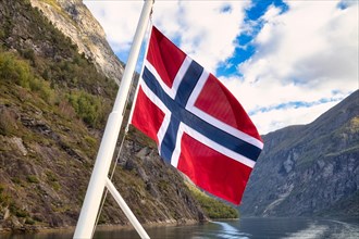 Norwegian flag in front of mountain panorama in Geirangerfjord near Geiranger
