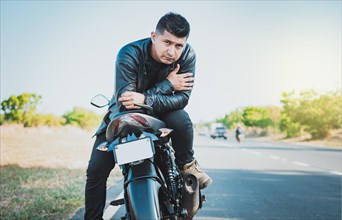 Portrait of handsome biker on his motorbike looking at camera outdoors