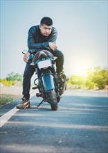 Handsome motorcyclist in jacket sitting on his motorcycle at the side of the road