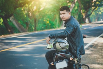 Latin motorcyclist sitting on his motorbike near an asphalt road
