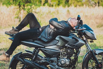 Motorcyclist in jacket lying on his motorcycle in the countryside