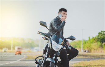 Biker sitting on motorcycle calling on the phone on the roadside