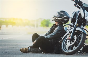 Biker sitting next to his motorcycle on the road