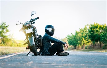 Male biker sitting next to his motorcycle on the road