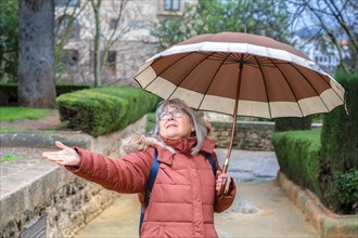 Elderly woman with umbrella on a rainy day holding out her hand to see if it is raining